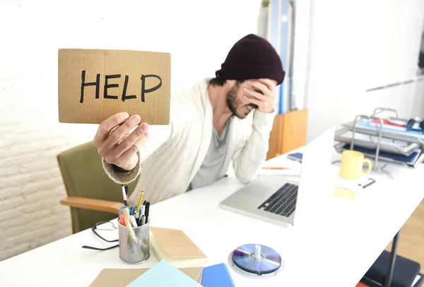 Обеспокоенный бизнесмен в прохладном хипстер шапочка взгляд холдинг помочь знак работает в стрессе в домашнем офисе — стоковое фото