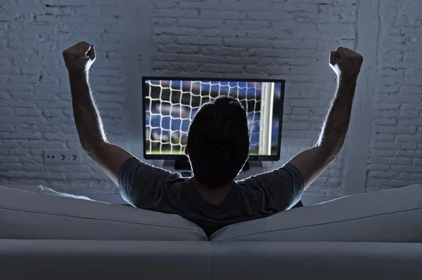 young man home alone watching soccer or football game in television enjoying and celebrating goal