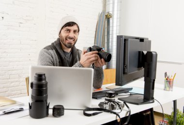 young attractive press photographer holding photographic camera viewing his work on editor office desk