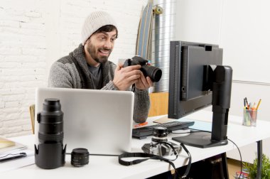 young attractive press photographer holding photographic camera viewing his work on editor office desk