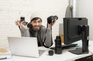 young attractive press photographer holding photographic camera viewing his work on editor office desk