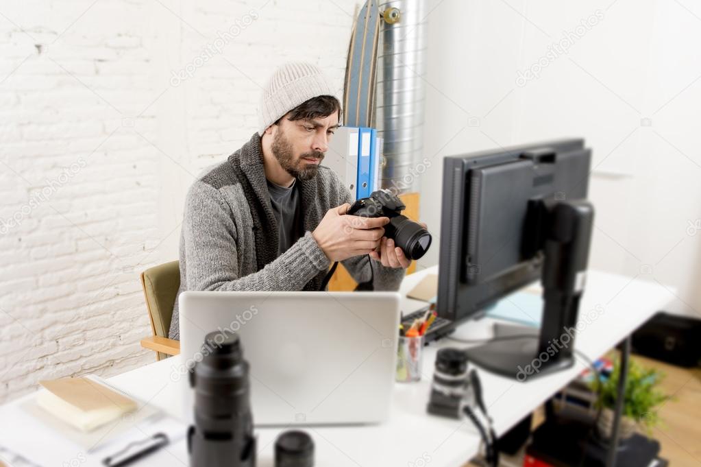 young attractive press photographer holding photographic camera viewing his work on editor office desk