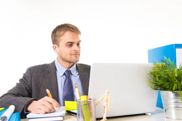 Молодий привабливий бізнесмен, який працює зайнятий ноутбуком на офісному столі, посміхаючись виглядати задоволеним — стокове фото