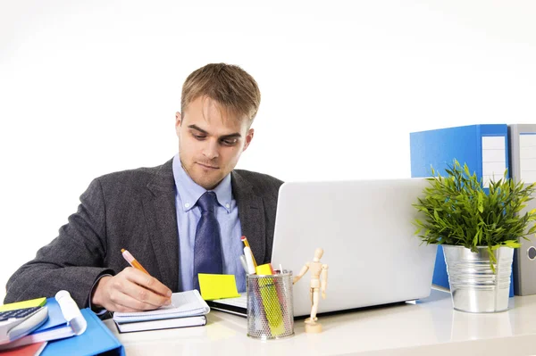 Homem de negócios atraente trabalhando ocupado com computador portátil escrevendo no pad com caneta na mesa de escritório — Fotografia de Stock