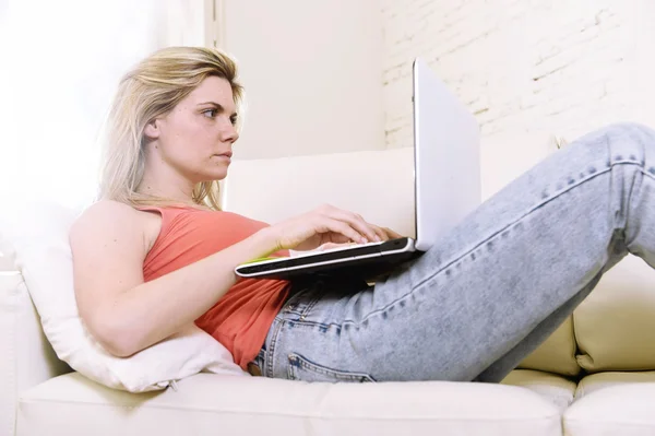 Young attractive blond hair woman lying comfortable on home sofa using internet in laptop computer — Stock Photo, Image