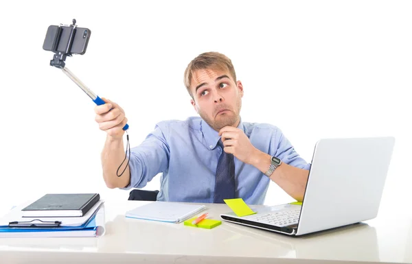 Hombre de negocios en camisa y corbata sentado en el escritorio de la computadora de la oficina sosteniendo el palo selfie que dispara foto del autorretrato —  Fotos de Stock
