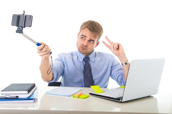 Hombre de negocios en camisa y corbata sentado en el escritorio de la computadora de la oficina sosteniendo el palo selfie que dispara foto del autorretrato —  Fotos de Stock