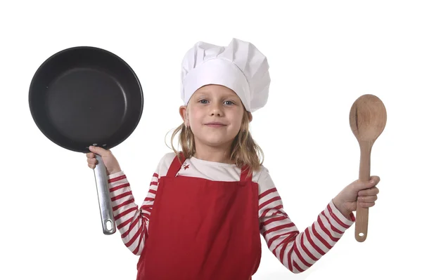 6 or 7 years old little girl in cooking hat and red apron playing cook smiling  happy holding pan and spoon — Stock Photo, Image