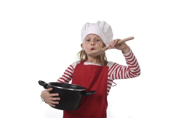 Little girl in cooking hat and red apron playing cook smiling  happy holding pot and pretending tasting food — Stock Photo, Image