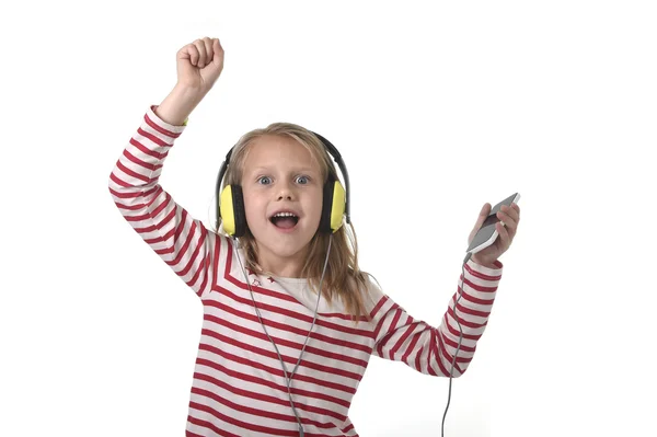 Dulce niña con cabello rubio escuchando música con auriculares y teléfono móvil cantando y bailando feliz —  Fotos de Stock