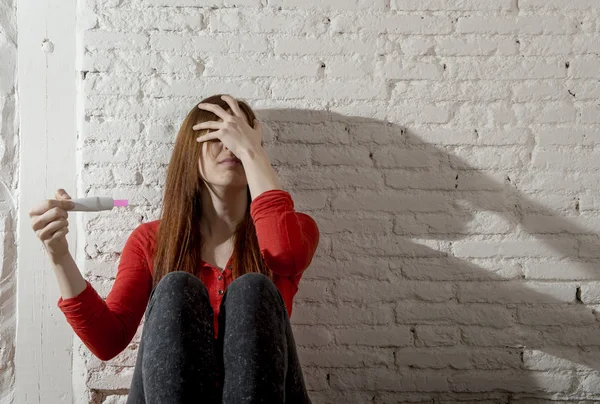 Scared worried pregnant teenager girl or young desperate woman holding positive pregnancy test Stock Image