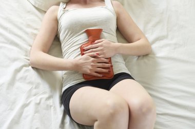 young woman suffering stomach cramps on belly holding hot water bottle against tummy clipart