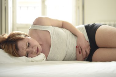 young beautiful woman suffering stomach cramps on belly holding tummy with her hands in period pain