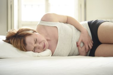 young beautiful woman suffering stomach cramps on belly holding tummy with her hands in period pain