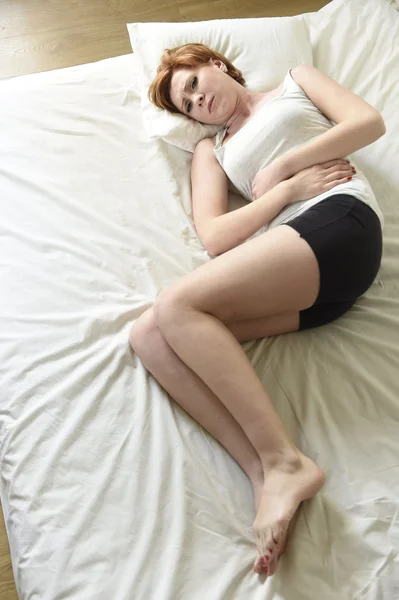 Young beautiful woman suffering stomach cramps on belly holding tummy with her hands in period pain — 图库照片