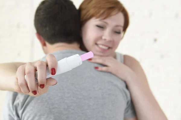 Молода щаслива жінка обіймає чоловіка, який тримає позитивний результат тест на вагітність, очікуючи дитину — стокове фото