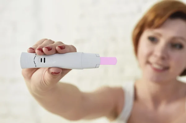 Young attractive pregnant woman holding happy positive result pregnancy test sitting on bed — Stockfoto