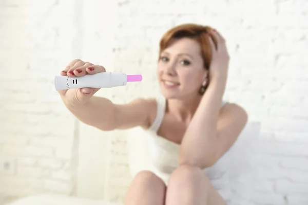 Young attractive pregnant woman holding happy positive result pregnancy test sitting on bed — Stok fotoğraf