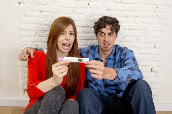 Young sad couple scared in shock and surprise reading pink positive pregnancy test overwhelmed in panic — Stock fotografie