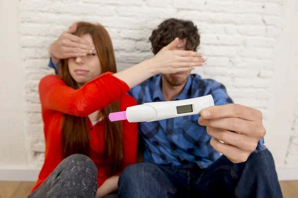 Young sad couple  in shock and surprise holding pink positive pregnancy test blocking eyes scared — Stok fotoğraf