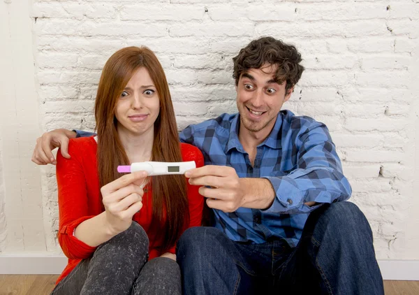 Young couple in shock and surprise with scared pregnant girl reading pink positive pregnancy — Stok fotoğraf