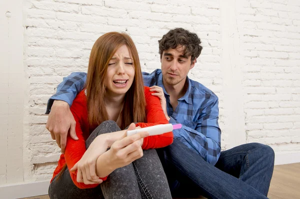 Young sad couple scared with pregnant girl reading pink positive pregnancy test crying overwhelmed — Stockfoto