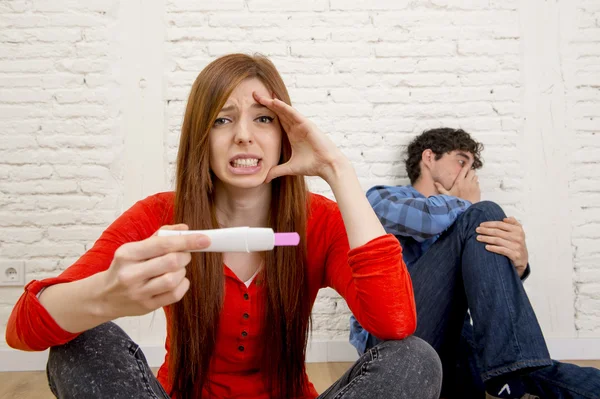 Young sad couple scared in shock and surprise reading pink positive pregnancy test overwhelmed in panic — Stockfoto