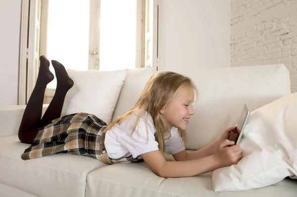 Blond little girl lying on home sofa couch using internet app on digital tablet pad on digital tablet pad — Stock Photo, Image