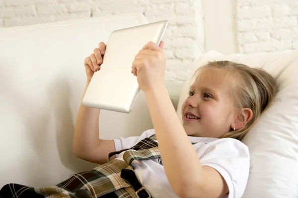 Blond little girl lying on home sofa couch using internet app on digital tablet pad on digital tablet pad — Stock Photo, Image