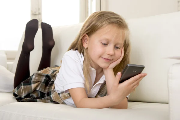 Boldog szőke kislány, segítségével internet-alkalmazás a mobil telefon haza kanapé — Stock Fotó
