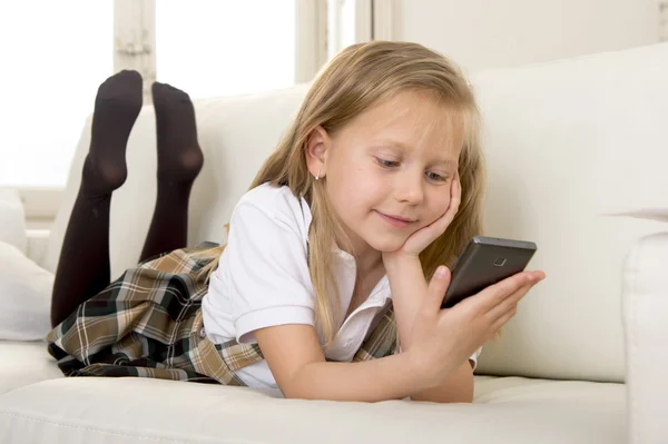 Happy blond little girl on home sofa using internet app on mobile phone — Stock Photo, Image