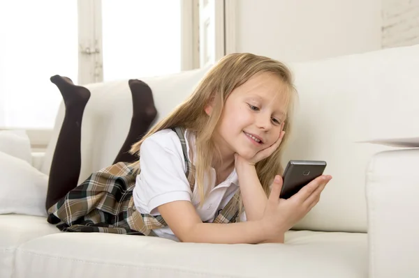 Felice bambina bionda sul divano di casa utilizzando l'app internet sul telefono cellulare — Foto Stock