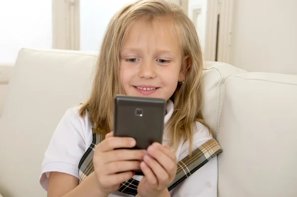 Niña rubia feliz en el sofá de casa utilizando la aplicación de Internet en el teléfono móvil — Foto de Stock