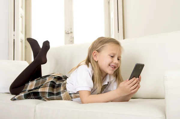 Criança do sexo feminino com cabelo loiro deitado em casa sofá usando o aplicativo de internet no telefone móvel — Fotografia de Stock