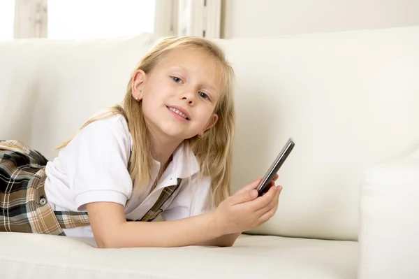 Niña con el pelo rubio acostada en el sofá de casa utilizando la aplicación de Internet en el teléfono móvil — Foto de Stock