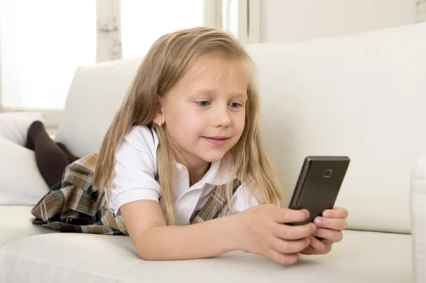 Девочка с светлыми волосами сидит на диване с помощью интернет-приложения на мобильном телефоне — стоковое фото