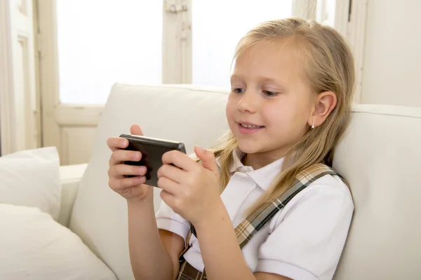 Niña con cabello rubio sentada en el sofá utilizando la aplicación de Internet en el teléfono móvil — Foto de Stock