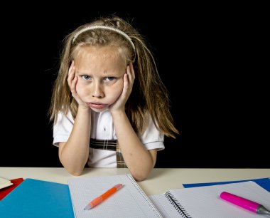 tired cute junior schoolgirl with blond hair sitting in stress working doing homework looking bored