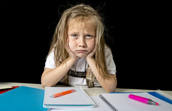 Müde niedliche Juniorschülerin mit blonden Haaren sitzt im Stress bei der Hausaufgabenarbeit und sieht gelangweilt aus — Stockfoto