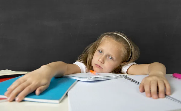 Müde niedliche Juniorschülerin mit blonden Haaren sitzt im Stress bei der Hausaufgabenarbeit und sieht gelangweilt aus — Stockfoto