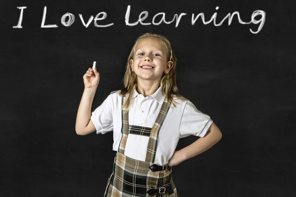 Sweet junior blond schoolgirl smiling happy in front of school classroom blackboard — Stock Photo, Image