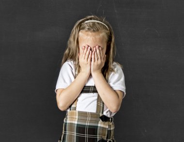 sweet junior schoolgirl with blonde hair crying sad and shy in front of school class blackboard 