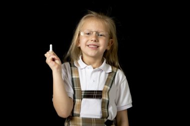 young sweet junior schoolgirl with blonde hair standing happy and smiling holding chalk