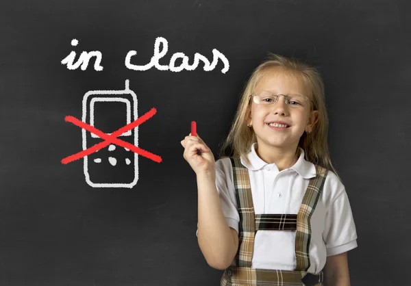 Young sweet junior schoolgirl writing with chalk about not using mobile phone in school class — Stockfoto