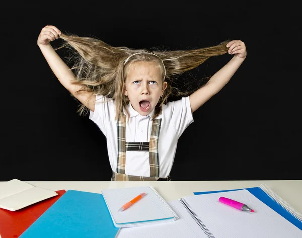 Crazy junior schoolgirl sitting on desk in stress working doing homework pulling her blond hair crazy — Stock Photo, Image