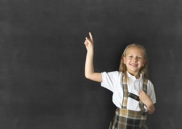 Colegiala junior con el pelo rubio de pie y sonriendo feliz apuntando a copiar el espacio en la pizarra de la clase — Foto de Stock