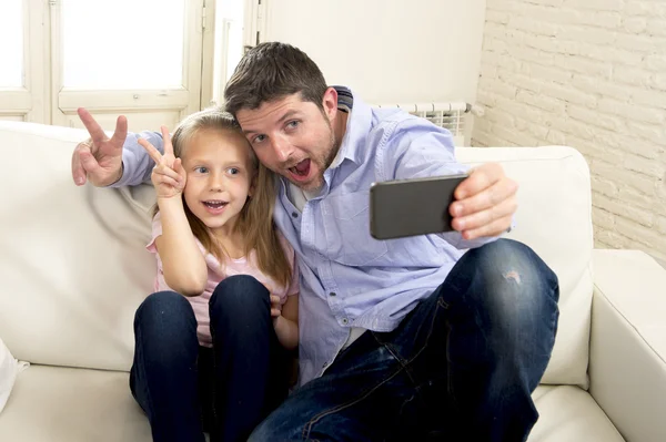 Young happy man having fun with his little cute blond daughter taking selfie photo with mobile phone — Stockfoto