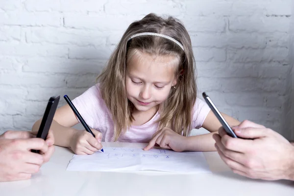 Маленькая девочка рисует в одиночестве, в то время как ее родители все время общаются на мобильном телефоне, игнорируя ее дочь — стоковое фото