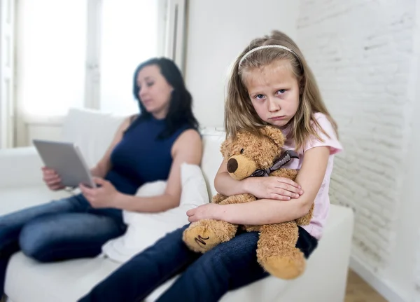 Young internet addict mother using digital tablet pad ignoring little sad daughter — Stock Photo, Image