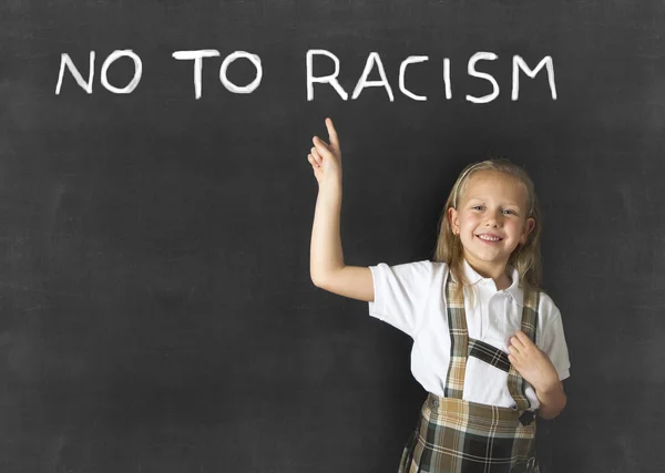 Junior uczennica z blond włosy wskazując palcem na tekst nie do rasizmu napisane w klasie tablica — Zdjęcie stockowe